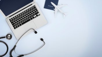 Reiseversicherungen für den Urlaub: Stethoskop, Laptop, Miniaturflugzeug mit Reisepass im Hintergrund.